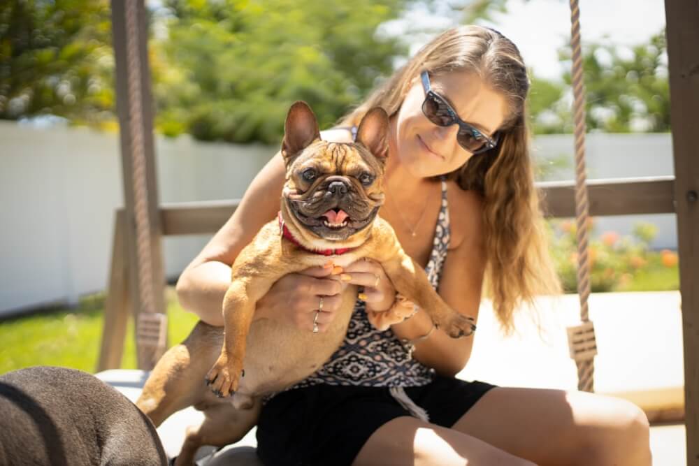 person kneeling in backyard training a French Bulldog to sit, treat held at nose level